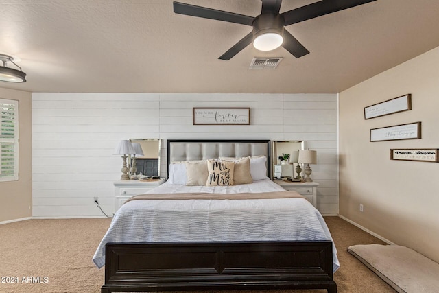 bedroom featuring ceiling fan, wood walls, light colored carpet, and a textured ceiling