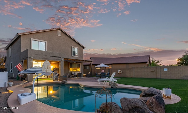 back house at dusk featuring a lawn, a patio area, and a fenced in pool