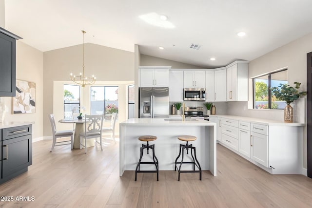 kitchen with lofted ceiling, appliances with stainless steel finishes, pendant lighting, light hardwood / wood-style floors, and white cabinets