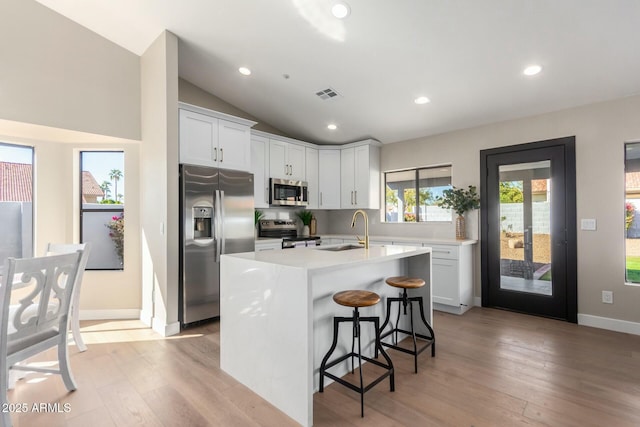 kitchen with a breakfast bar, sink, white cabinetry, appliances with stainless steel finishes, and an island with sink