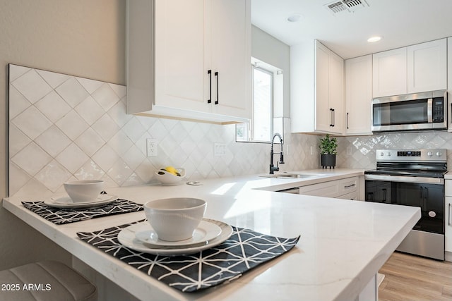 kitchen featuring sink, light hardwood / wood-style flooring, appliances with stainless steel finishes, light stone counters, and white cabinets