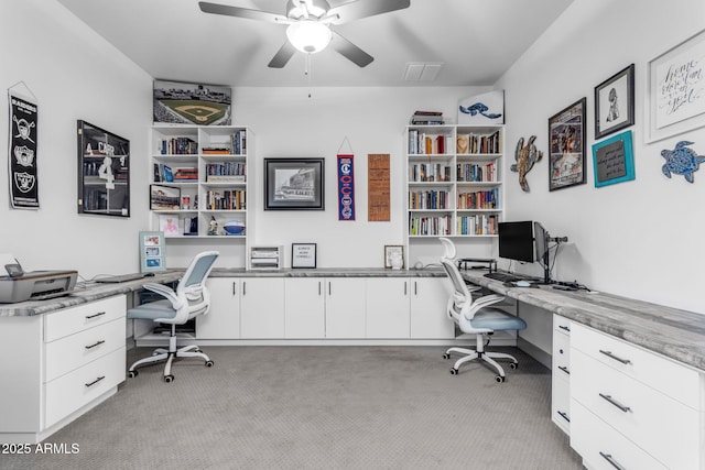 carpeted home office with ceiling fan and built in desk