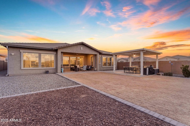 back house at dusk with ceiling fan and a patio