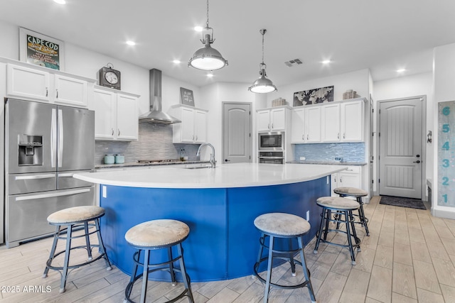 kitchen featuring a kitchen bar, wall chimney range hood, stainless steel appliances, white cabinets, and a spacious island