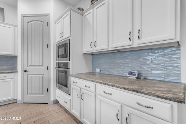 kitchen featuring built in microwave, white cabinetry, tasteful backsplash, and stainless steel oven