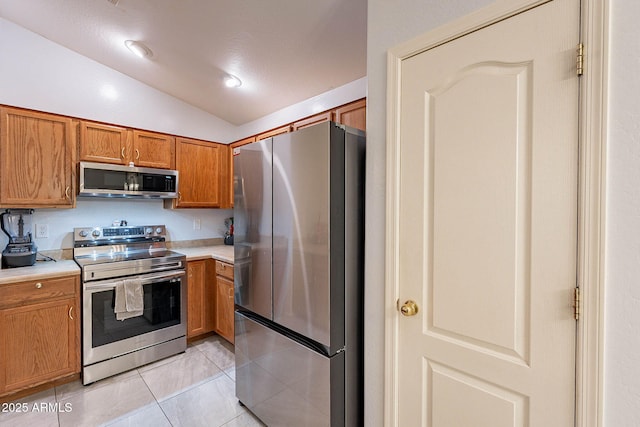 kitchen with stainless steel appliances, vaulted ceiling, and light tile patterned flooring