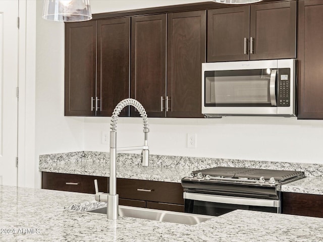 kitchen with dark brown cabinetry, light stone countertops, sink, and appliances with stainless steel finishes