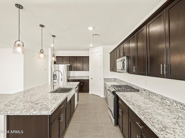 kitchen with dark brown cabinetry, sink, stainless steel appliances, pendant lighting, and a kitchen island with sink