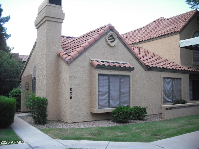 view of home's exterior with a tiled roof, a chimney, and stucco siding