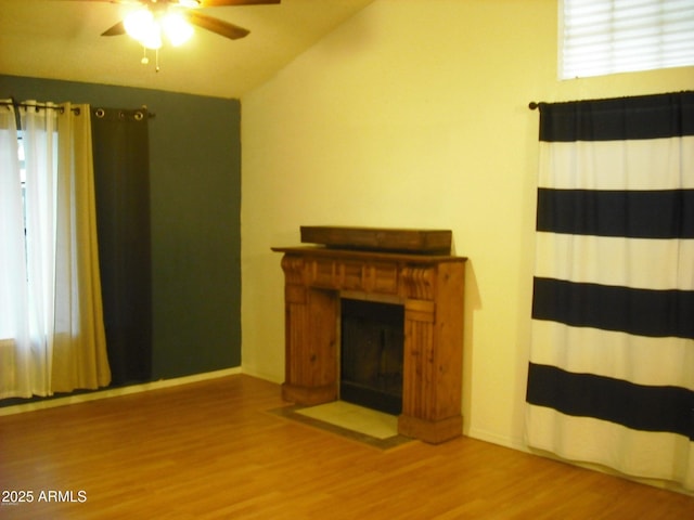 unfurnished living room with a fireplace with flush hearth, lofted ceiling, a ceiling fan, and wood finished floors