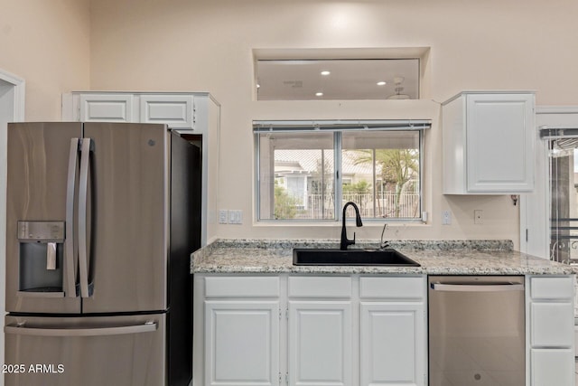 kitchen featuring light stone counters, appliances with stainless steel finishes, white cabinetry, and a sink