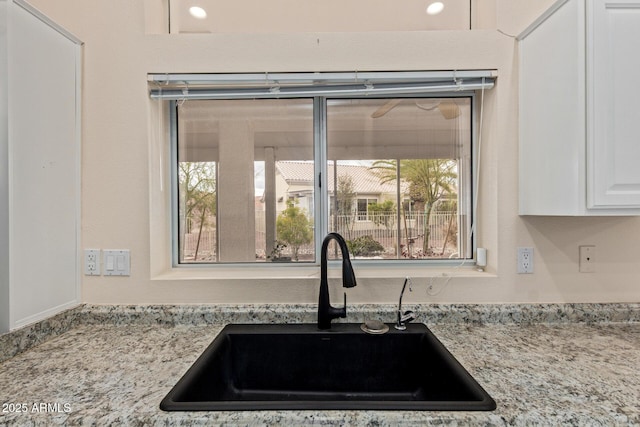 room details featuring a sink, light stone counters, and white cabinets