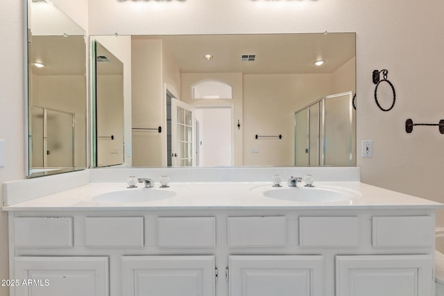 bathroom featuring a shower stall, double vanity, visible vents, and a sink