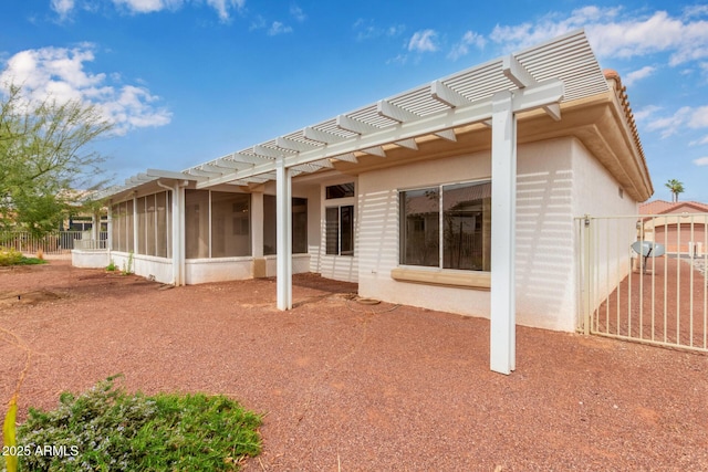 rear view of house featuring stucco siding, a sunroom, a pergola, and fence