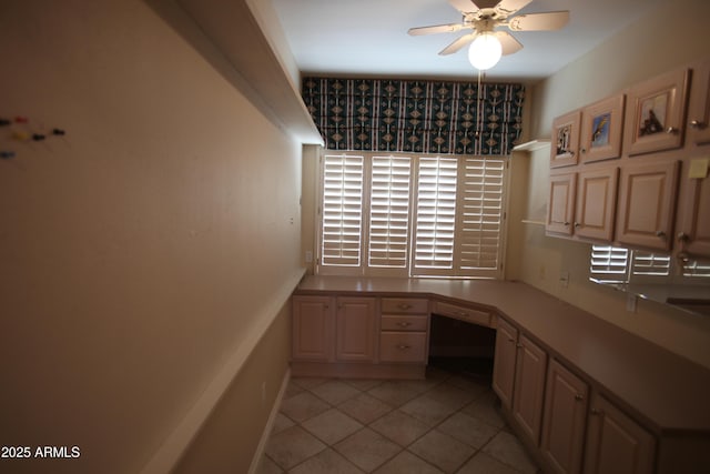 unfurnished office with light tile patterned floors, built in desk, a ceiling fan, and baseboards