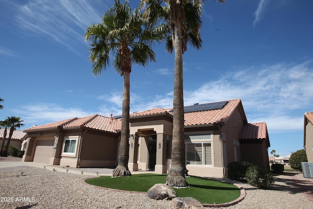 mediterranean / spanish house featuring a garage, roof mounted solar panels, a tiled roof, and stucco siding