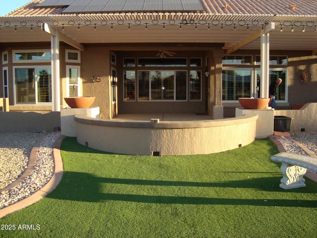 rear view of house featuring a tile roof, a ceiling fan, stucco siding, roof mounted solar panels, and a patio area