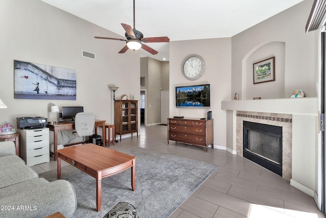 living room featuring ceiling fan, a towering ceiling, and a tile fireplace