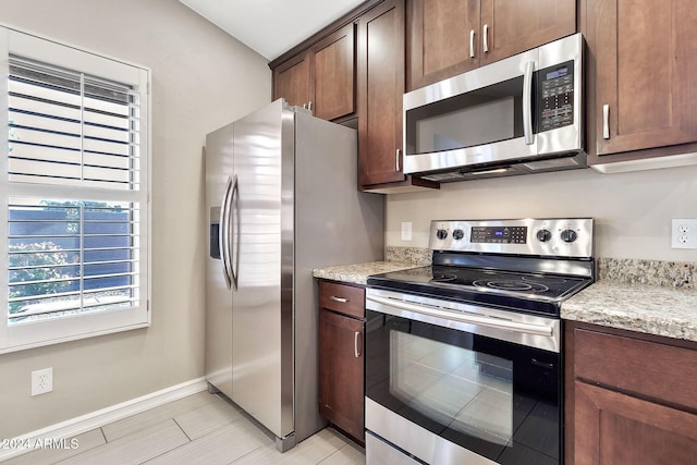 kitchen featuring dark brown cabinets, stainless steel appliances, and light stone counters