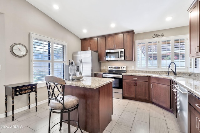 kitchen with lofted ceiling, sink, light stone countertops, a kitchen island, and stainless steel appliances