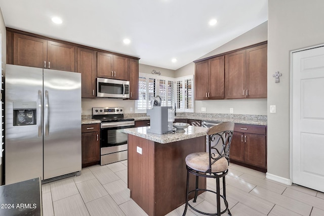 kitchen with dark brown cabinetry, light stone counters, vaulted ceiling, a kitchen island, and appliances with stainless steel finishes