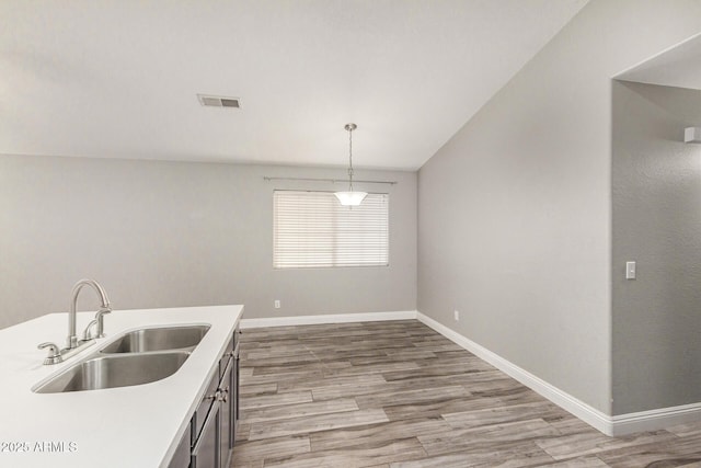 kitchen featuring pendant lighting, sink, lofted ceiling, and light wood-type flooring