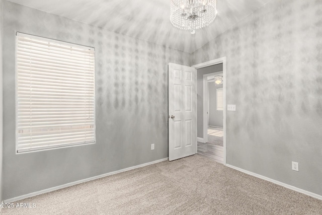 empty room featuring an inviting chandelier, carpet, and a wealth of natural light