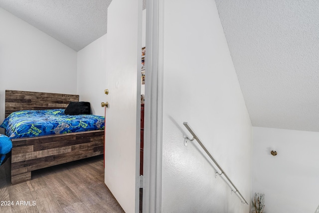 bedroom with a textured ceiling, vaulted ceiling, and hardwood / wood-style flooring