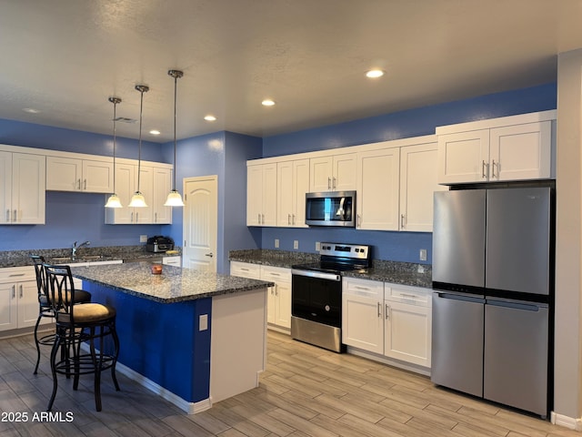 kitchen featuring white cabinetry, stainless steel appliances, decorative light fixtures, dark stone counters, and a center island