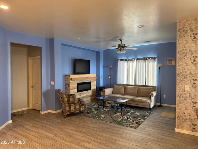 living room with light wood-type flooring, ceiling fan, and a fireplace