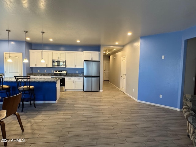 kitchen with white cabinets, appliances with stainless steel finishes, a kitchen island, decorative light fixtures, and dark stone counters