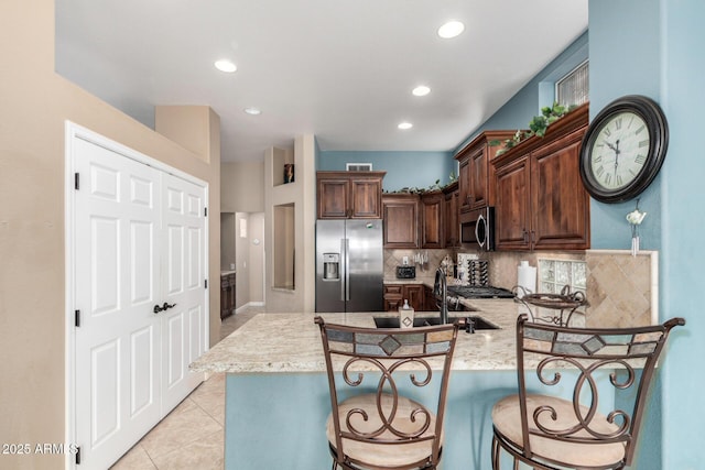 kitchen featuring appliances with stainless steel finishes, backsplash, kitchen peninsula, light tile patterned floors, and a breakfast bar area