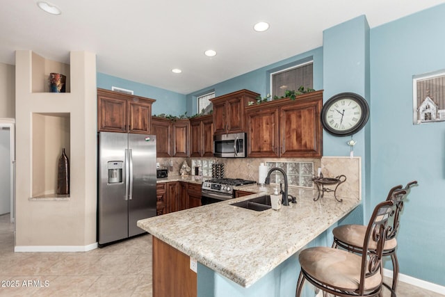 kitchen featuring light stone countertops, stainless steel appliances, decorative backsplash, sink, and kitchen peninsula