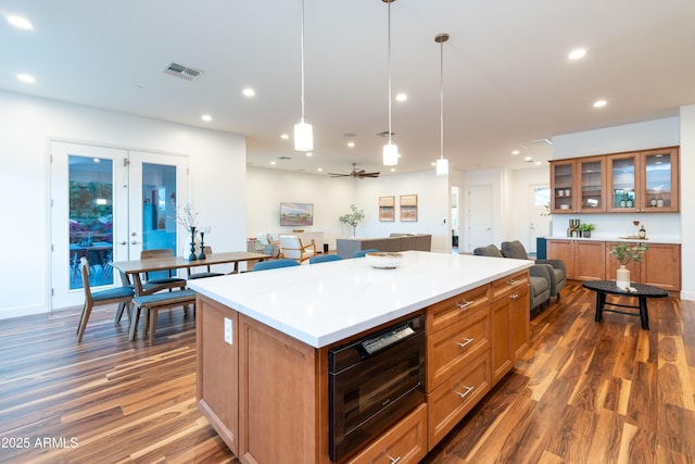 kitchen featuring glass insert cabinets, open floor plan, a center island, hanging light fixtures, and light countertops