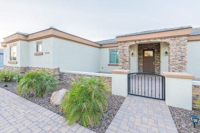 view of front of home featuring a gate, stone siding, and stucco siding