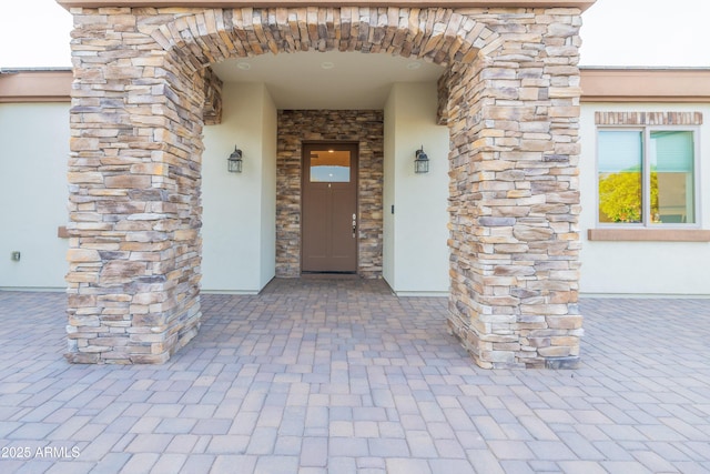 view of exterior entry featuring stone siding and stucco siding