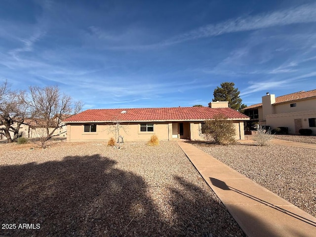 rear view of house with stucco siding, a chimney, and a tiled roof