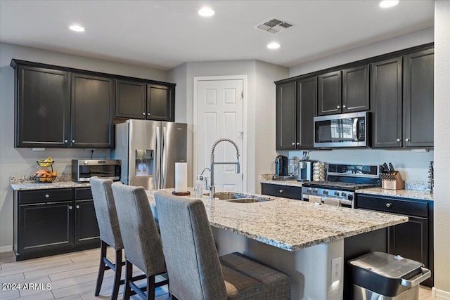 kitchen featuring a breakfast bar, appliances with stainless steel finishes, light wood-type flooring, and a kitchen island with sink