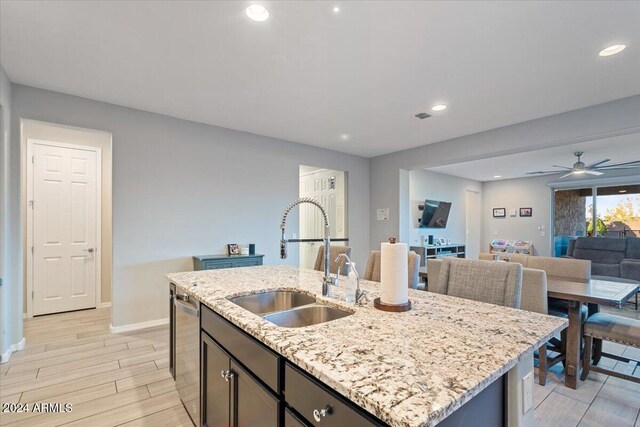 kitchen with stainless steel dishwasher, ceiling fan, sink, a center island with sink, and light hardwood / wood-style flooring