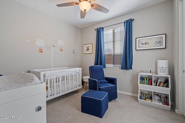 bedroom featuring a crib, light colored carpet, and ceiling fan