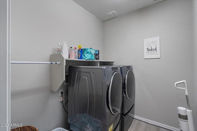 washroom featuring washing machine and clothes dryer, light hardwood / wood-style floors, and a textured ceiling