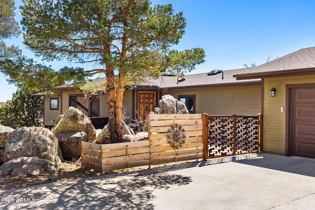 view of front of home featuring driveway, a garage, fence, and a shingled roof