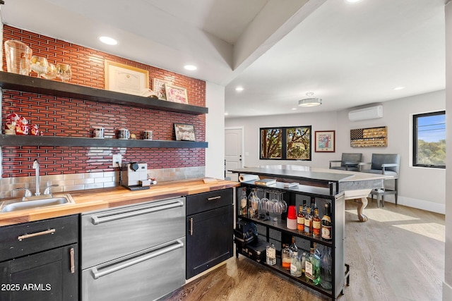bar featuring a wall mounted AC, baseboards, tasteful backsplash, a sink, and light wood-style floors