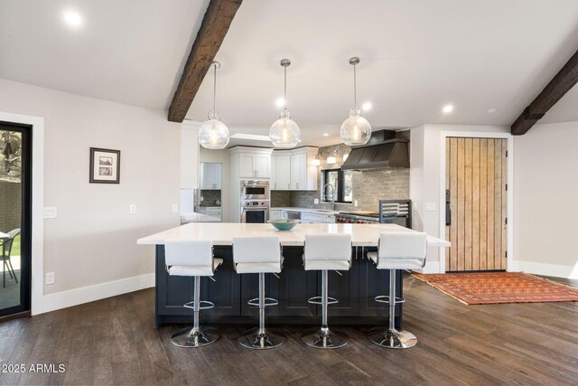 kitchen featuring light countertops, a sink, wall chimney exhaust hood, tasteful backsplash, and beamed ceiling