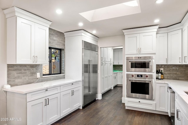 kitchen featuring white cabinetry, a skylight, appliances with stainless steel finishes, and backsplash