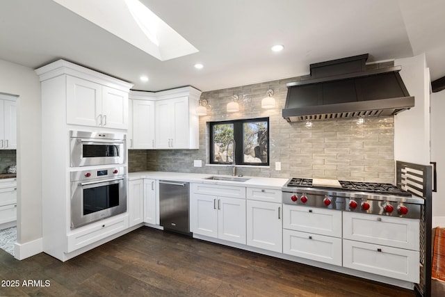 kitchen featuring a sink, wall chimney exhaust hood, a skylight, appliances with stainless steel finishes, and dark wood-type flooring