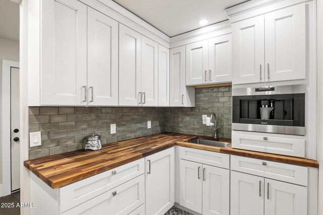 kitchen featuring wooden counters, white cabinets, decorative backsplash, and a sink