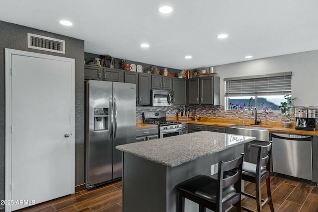 kitchen featuring a breakfast bar, sink, a center island, stainless steel appliances, and light stone countertops