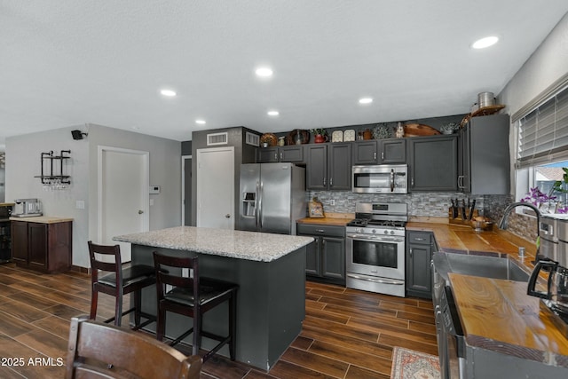 kitchen with a kitchen island, tasteful backsplash, gray cabinetry, a kitchen bar, and stainless steel appliances