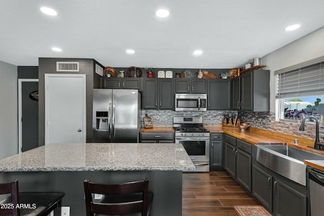 kitchen featuring appliances with stainless steel finishes, sink, a breakfast bar area, backsplash, and light stone countertops